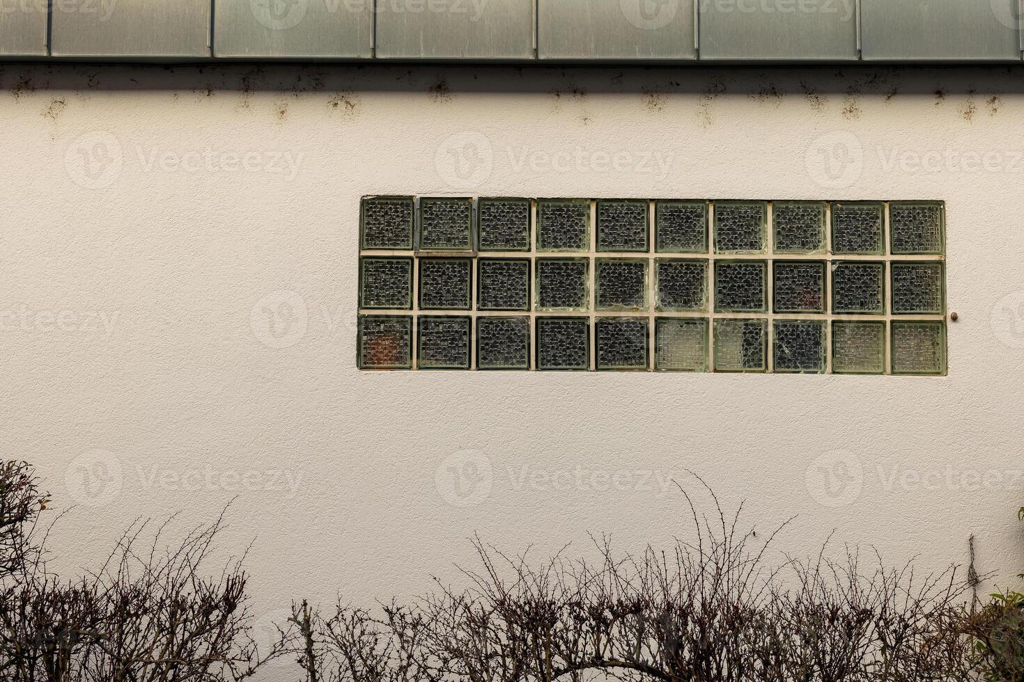 Glass block window adorned with fading graffiti on a plain wall in an urban setting during daylight photo