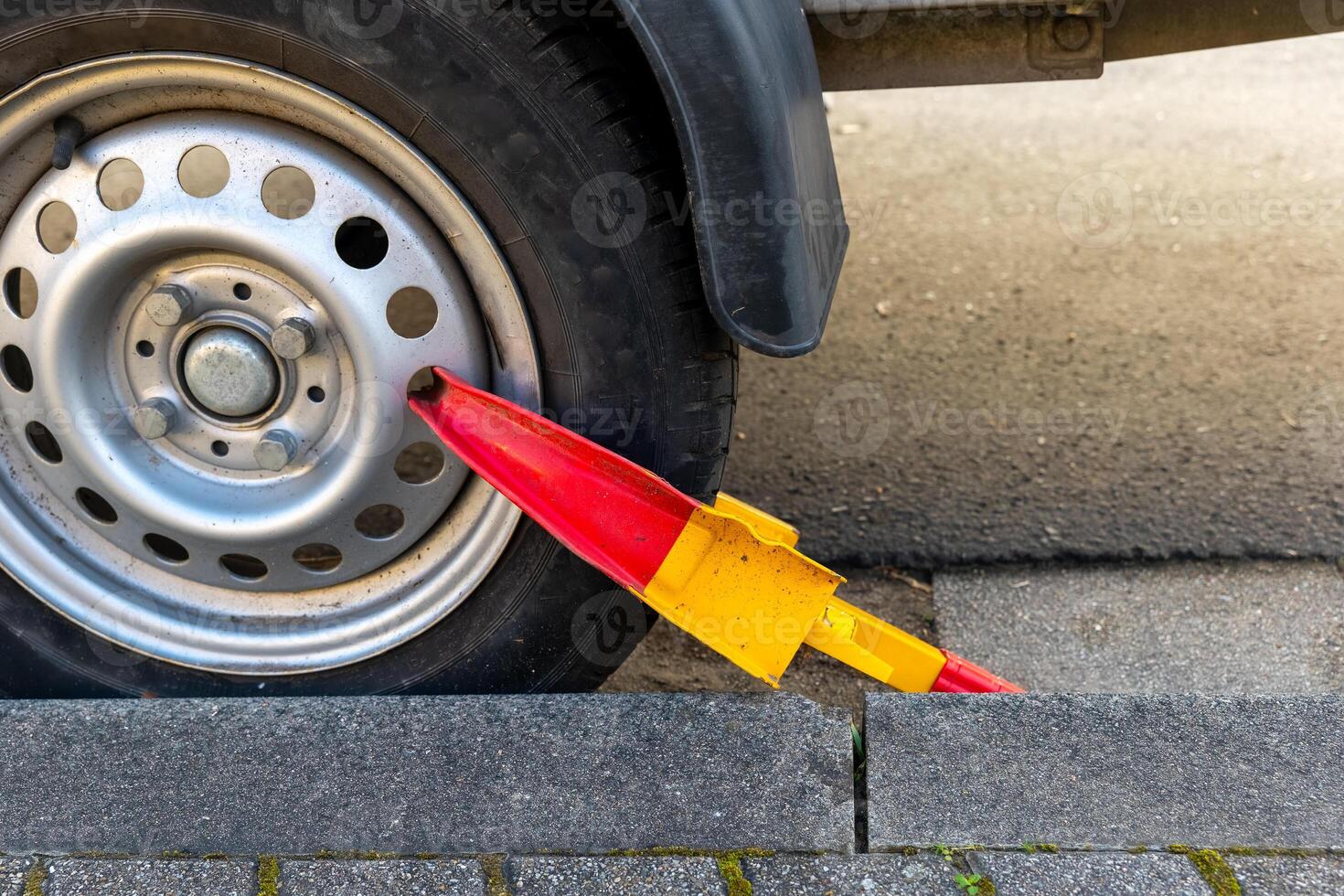 Vehicle immobilization device attached to tire on city street during daylight hours for preventing unauthorized parking photo