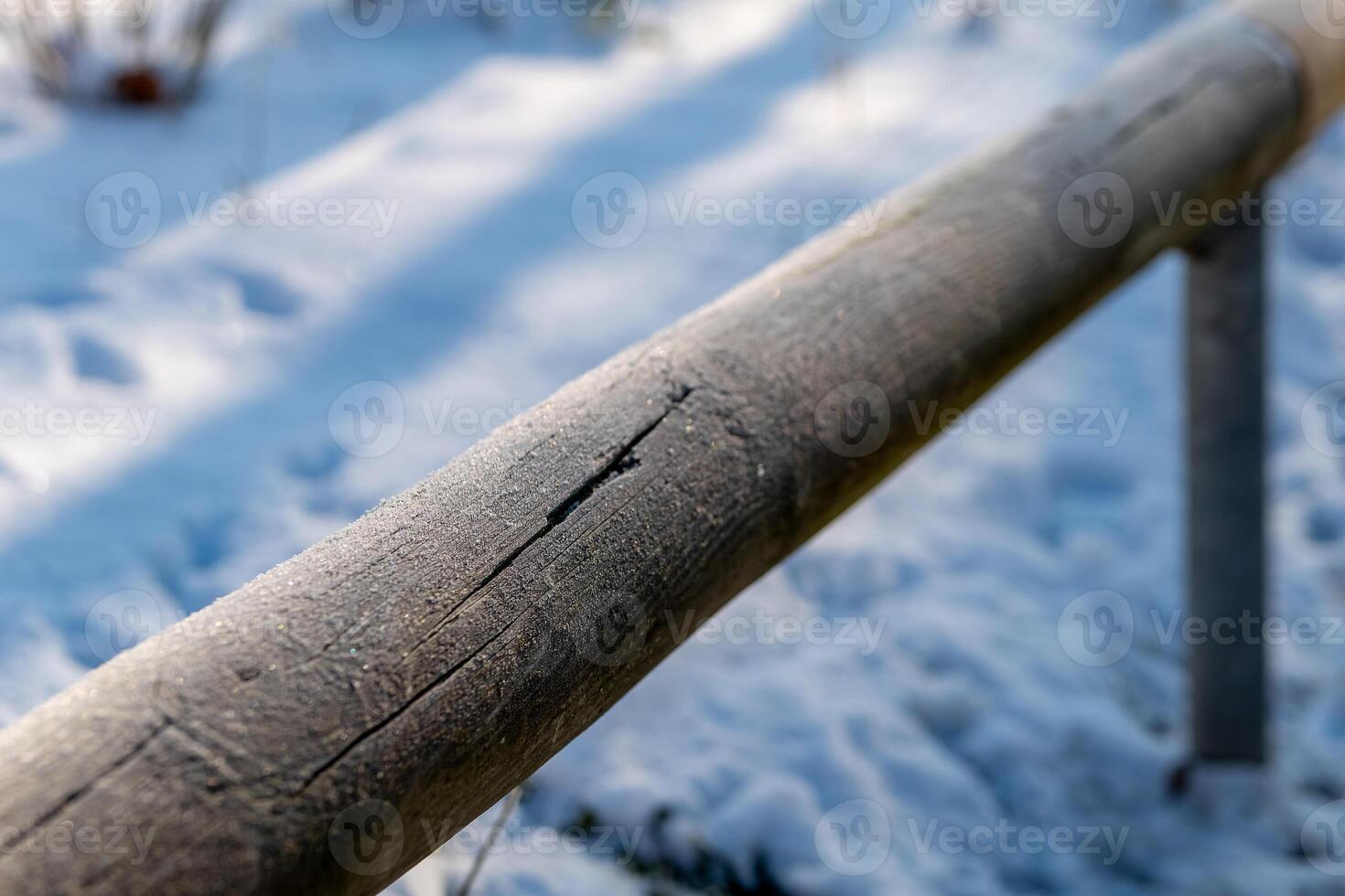 Frost-covered wooden railing in a tranquil winter landscape under soft sunlight photo