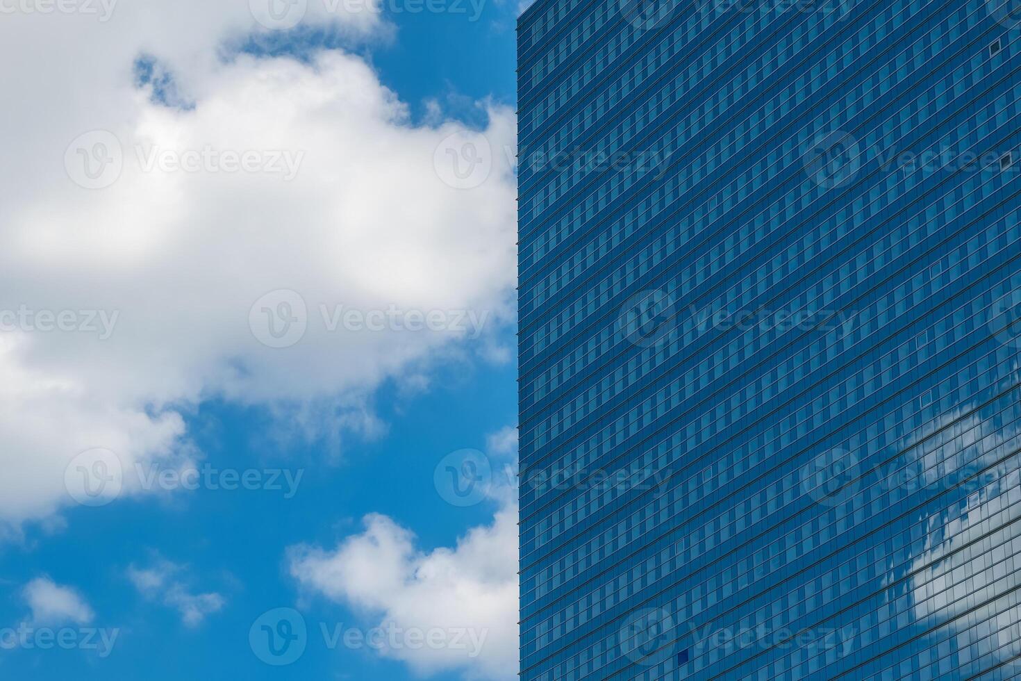 Modern glass building reflects clouds in a clear blue sky during a sunny day in an urban environment photo