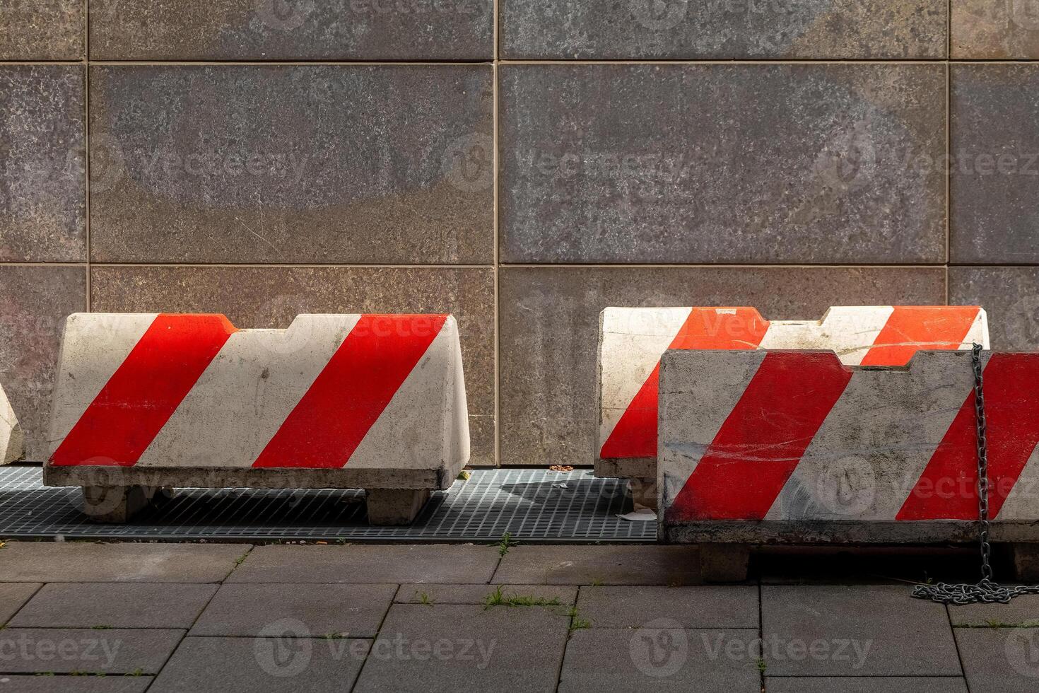 Concrete barriers line the pavement near a textured wall during daylight in an urban environment photo