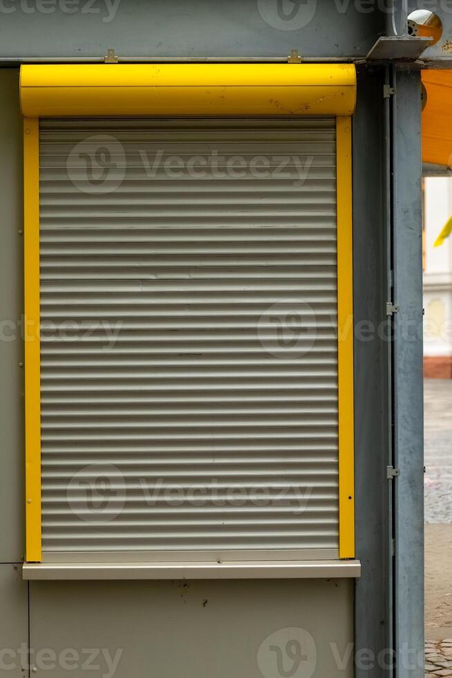 Shuttered kiosk with metallic roll-down door and bright yellow trim in an urban setting at noon photo