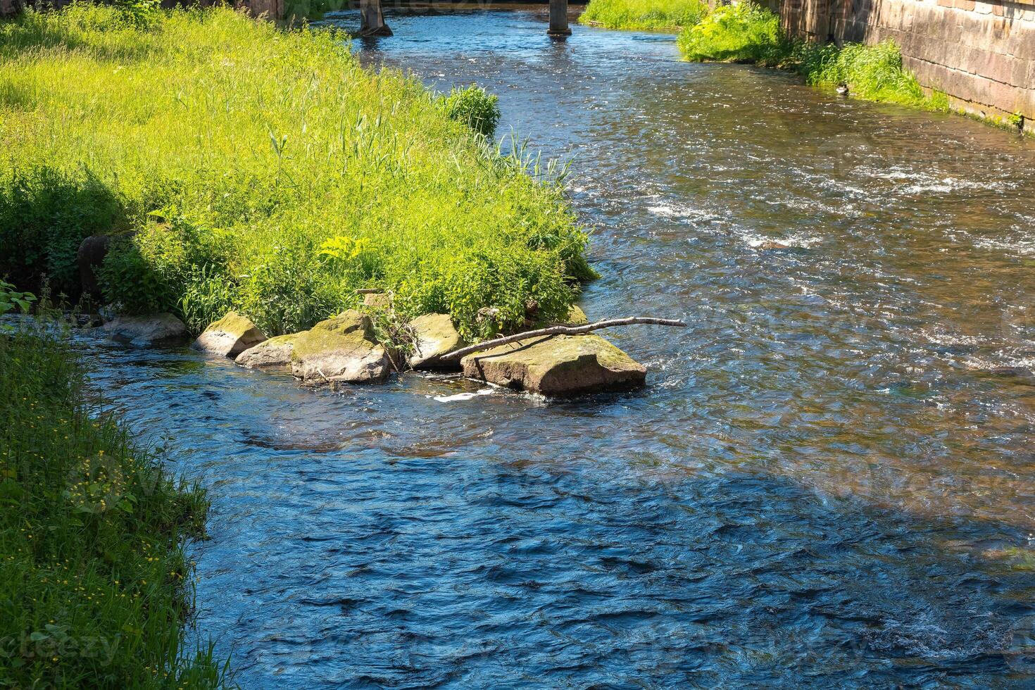 Flowing river surrounded by lush green vegetation under bright sunlight in a tranquil setting photo