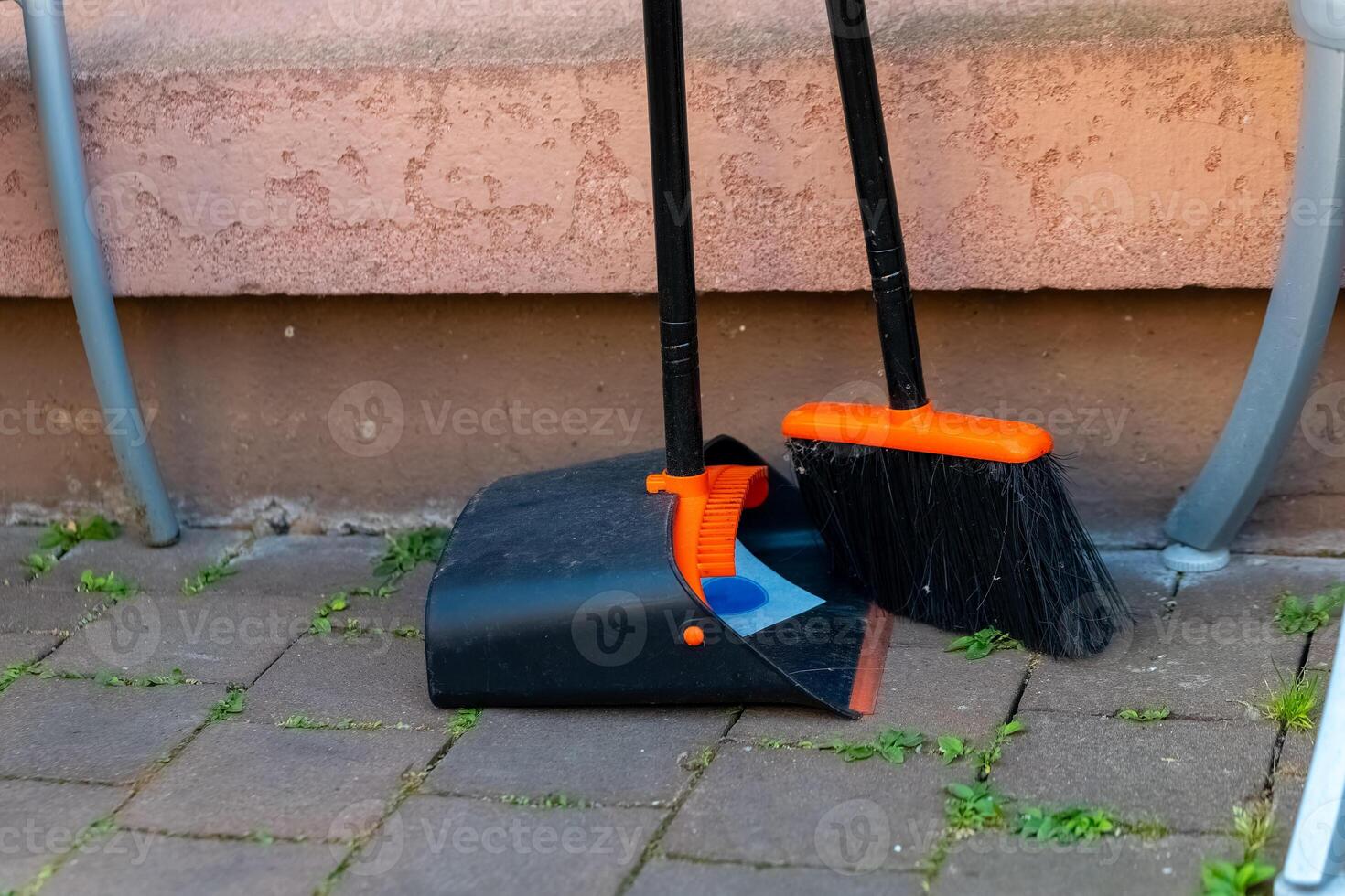 Cleaning tools resting on a porch with green grass peeking through the pavement at a sunny moment photo