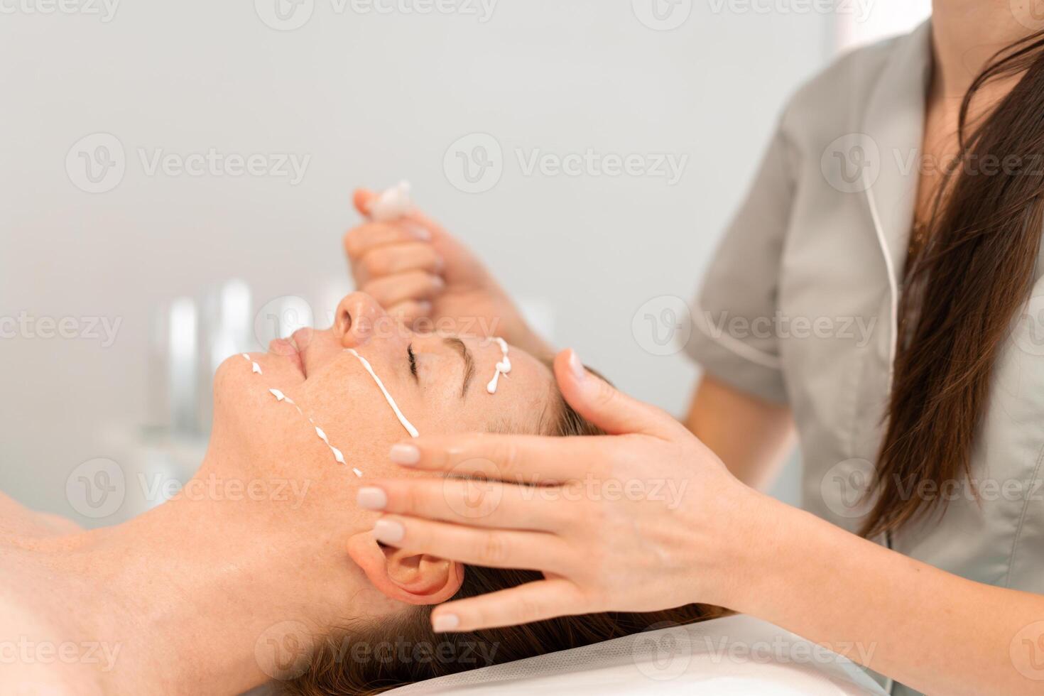 Massage therapist applying face cream to relaxed woman at salon photo