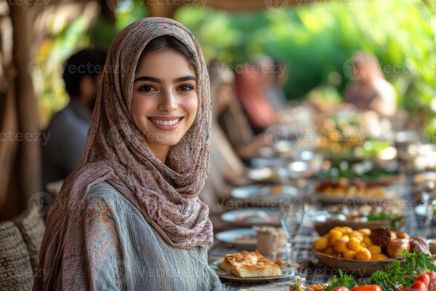 A woman wearing a headscarf sitting at a table with food photo