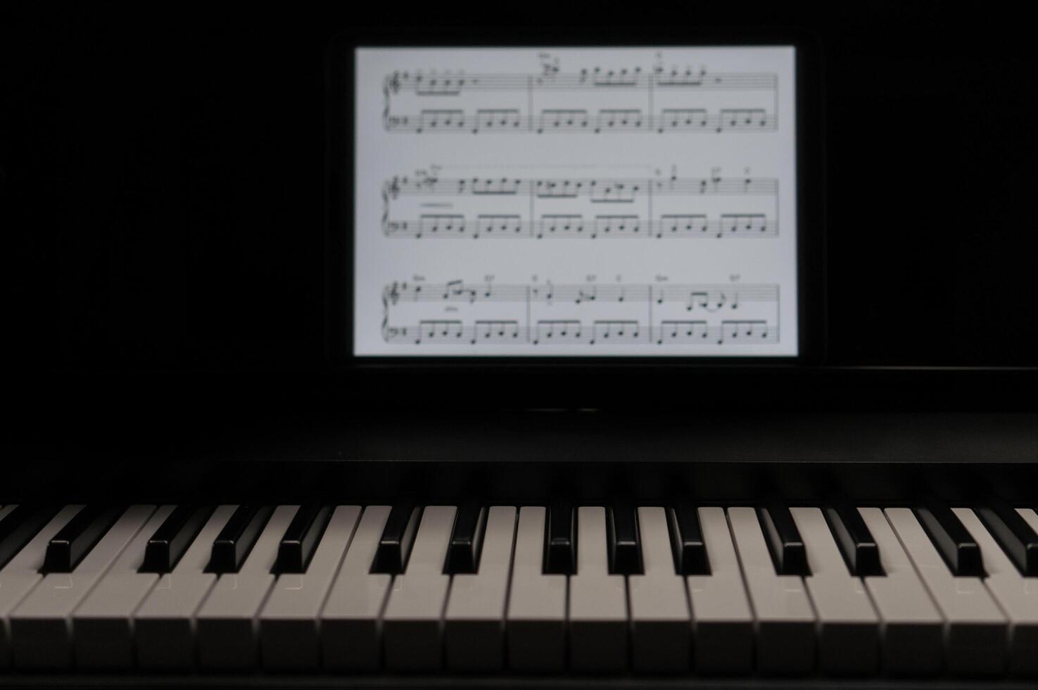 Front view of the black and white keys of an electric piano and tablet screen. photo