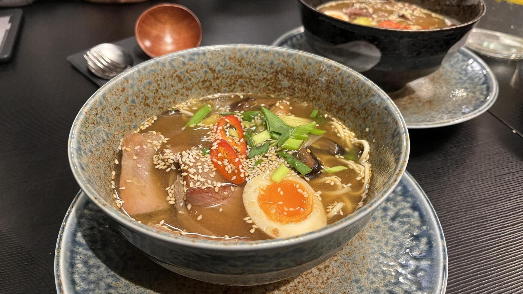 Close-up of a bowl beef ramen with a soft-boiled egg, vegetables, and sesame seeds in a cozy Japanese restaurant photo