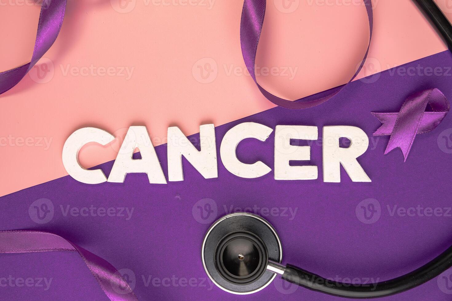 A stethoscope lies next to the word CANCER spelled out in white letters and a purple ribbon. International cancer day concept photo