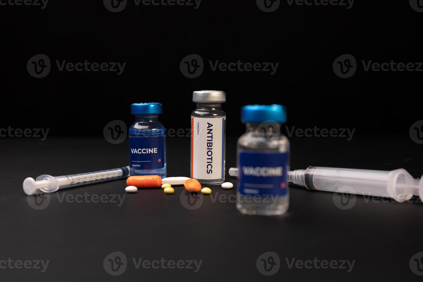 Two vaccine vials and one antibiotics vial sit next to two syringes and several pills. Health and medical concept photo