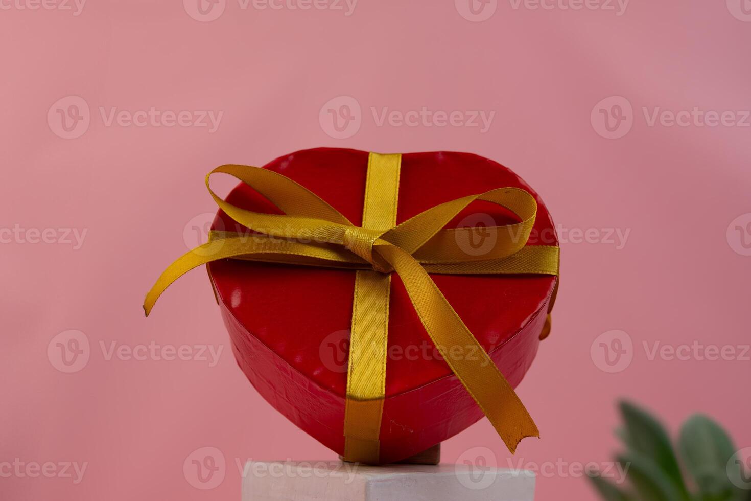 A heart shaped red box with a gold ribbon sitting on a surface photo