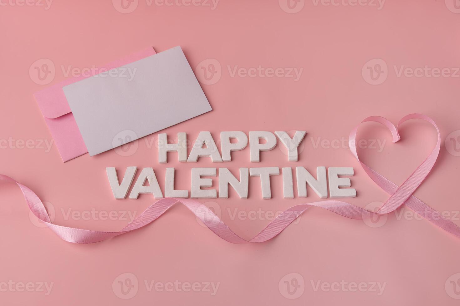 A pink ribbon forming a heart shape next to an envelope and the words Happy Valentine photo