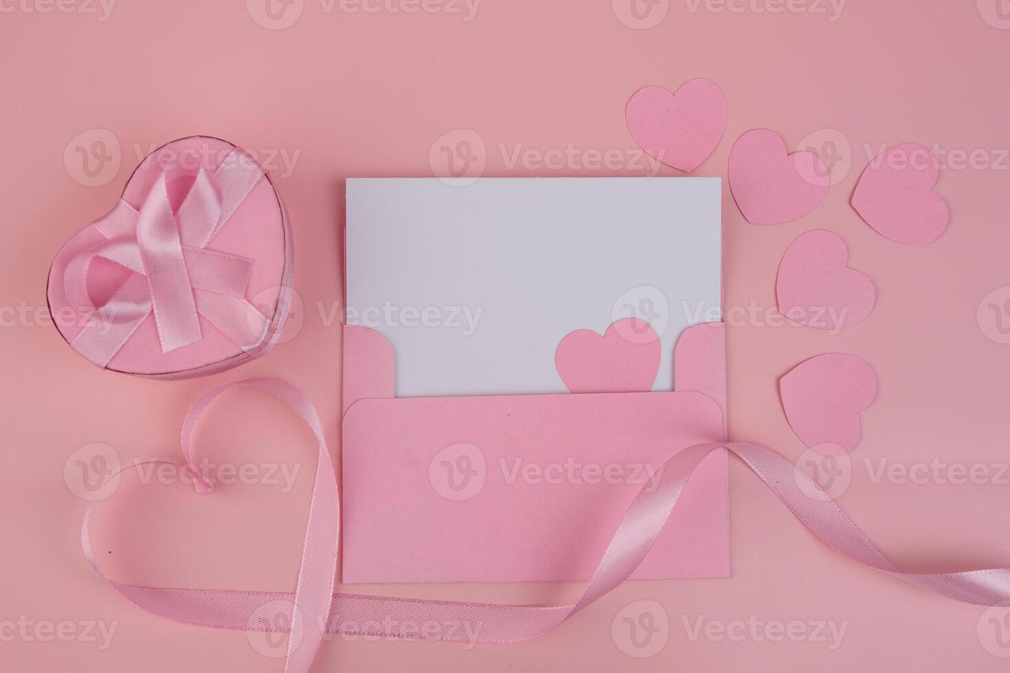 A pink heart shaped gift box and envelope with a blank card inside surrounded by pink hearts and ribbon photo