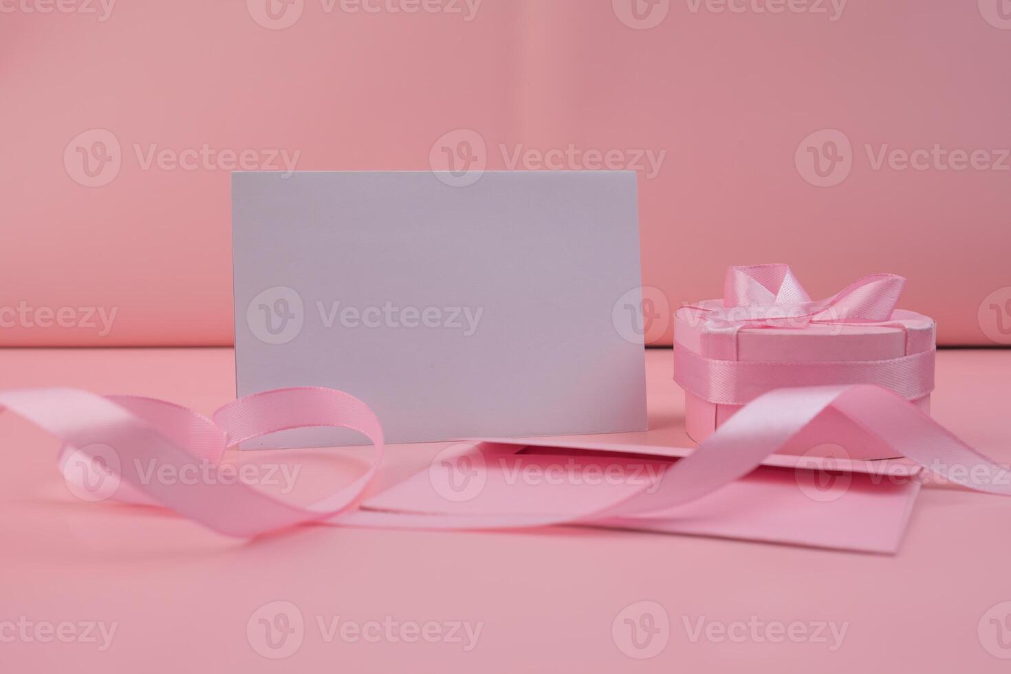 A pink ribbon rests beside a blank card and a pink gift box photo