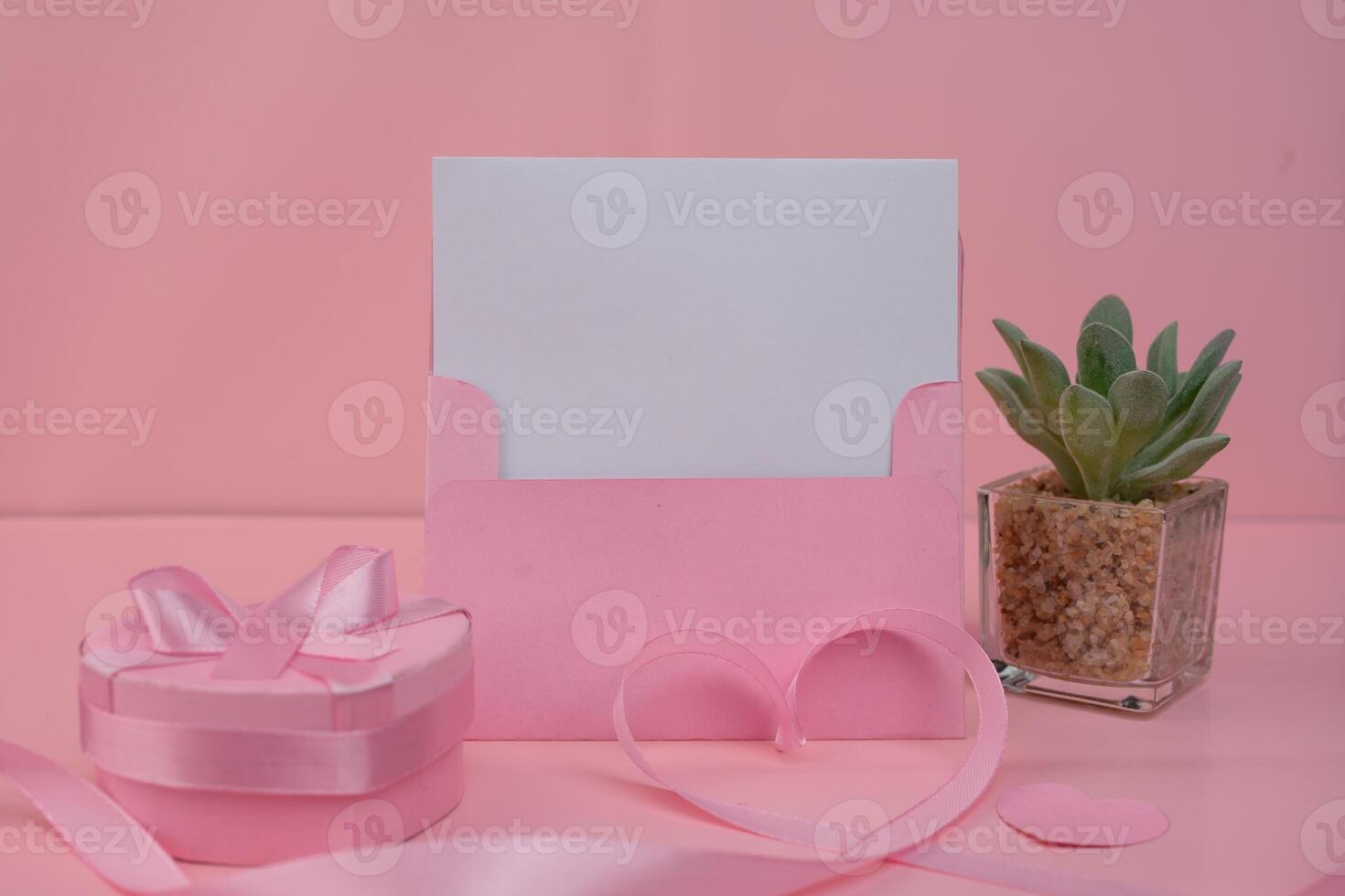 A pink envelope holding a blank card sits next to a pink gift box with a ribbon. invitation mockup concept photo