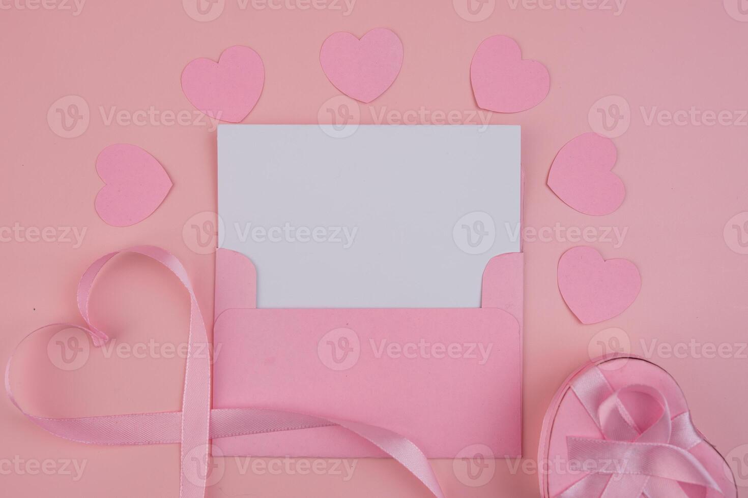 A pink envelope containing a blank card surrounded by pink hearts and a heart shaped ribbon and gift photo