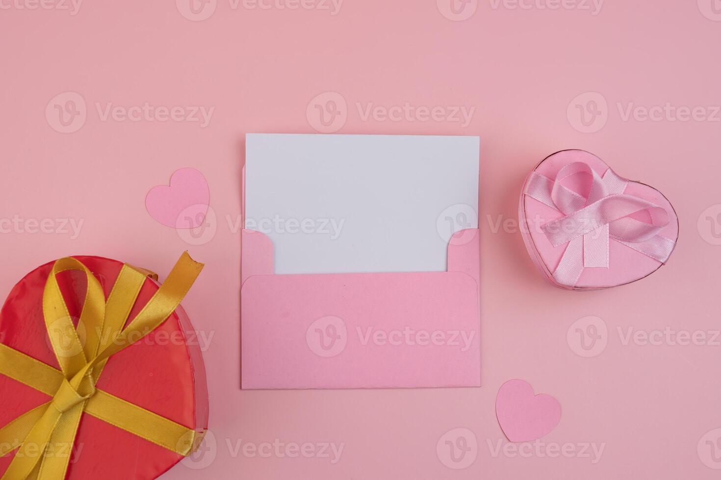 A pink envelope holding a blank card sits beside a red heart shaped gift box and a pink heart shaped gift box. invitation mockup photo