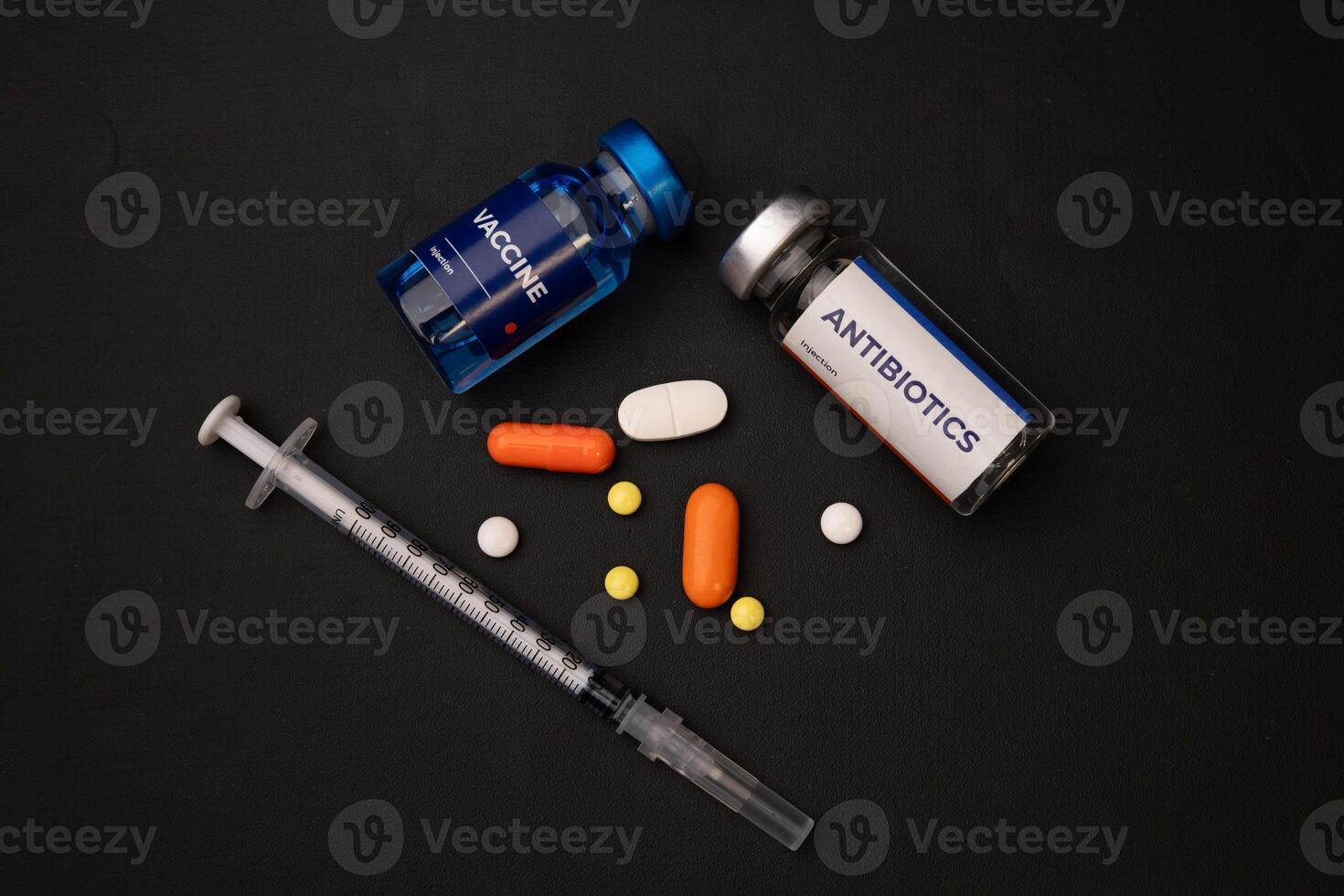 A syringe vaccine vial antibiotics vial and pills are lying on a dark surface. health and medical concept photo