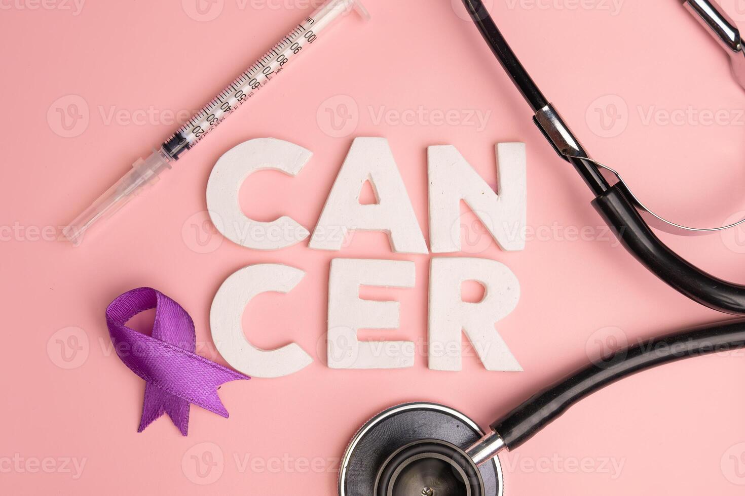 A syringe stethoscope and purple ribbon are arranged around the word CANCER. World cancer day concept photo