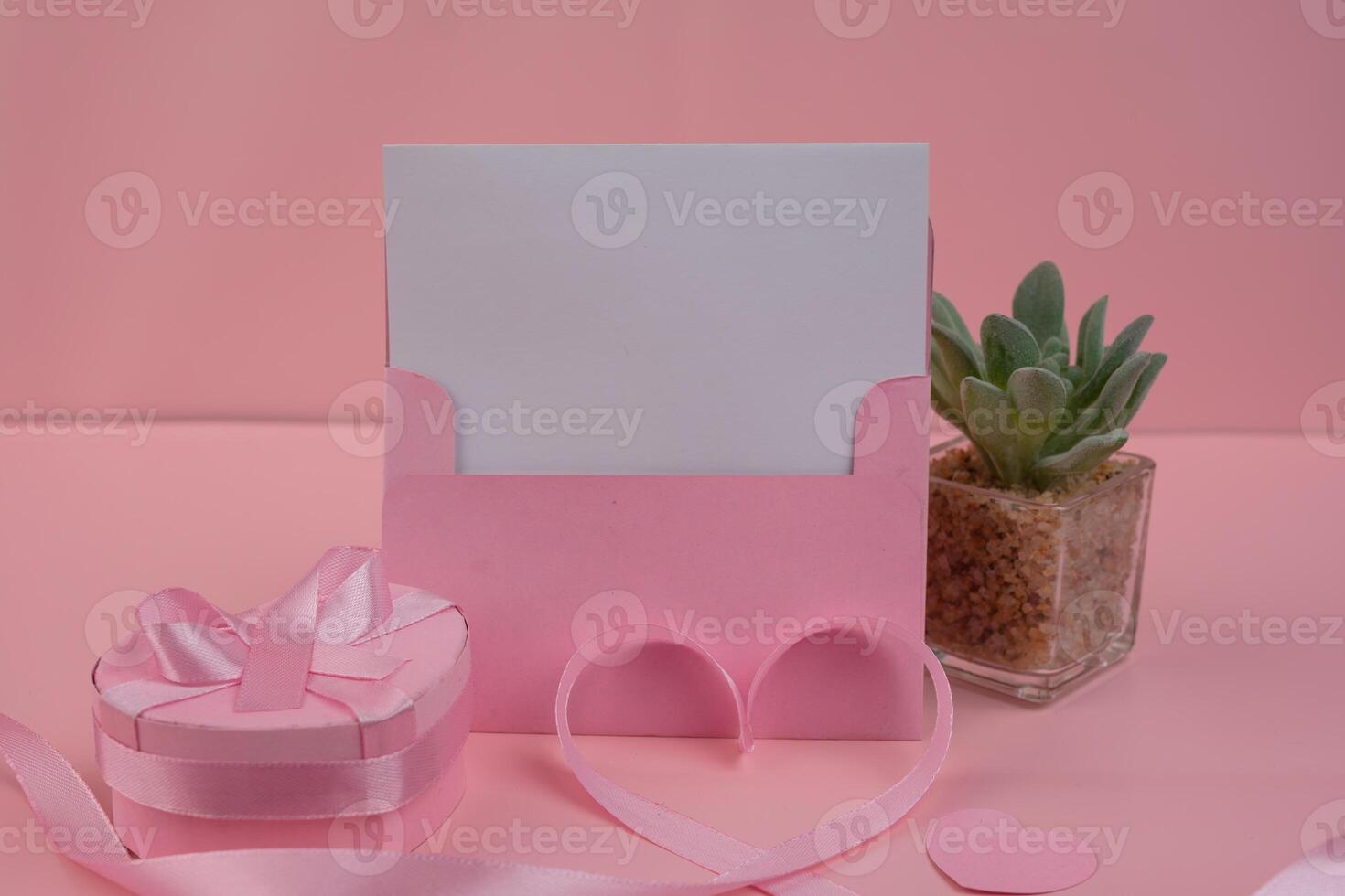 A pink envelope holding a blank card sits next to a heart shaped gift box. invitation mockup photo