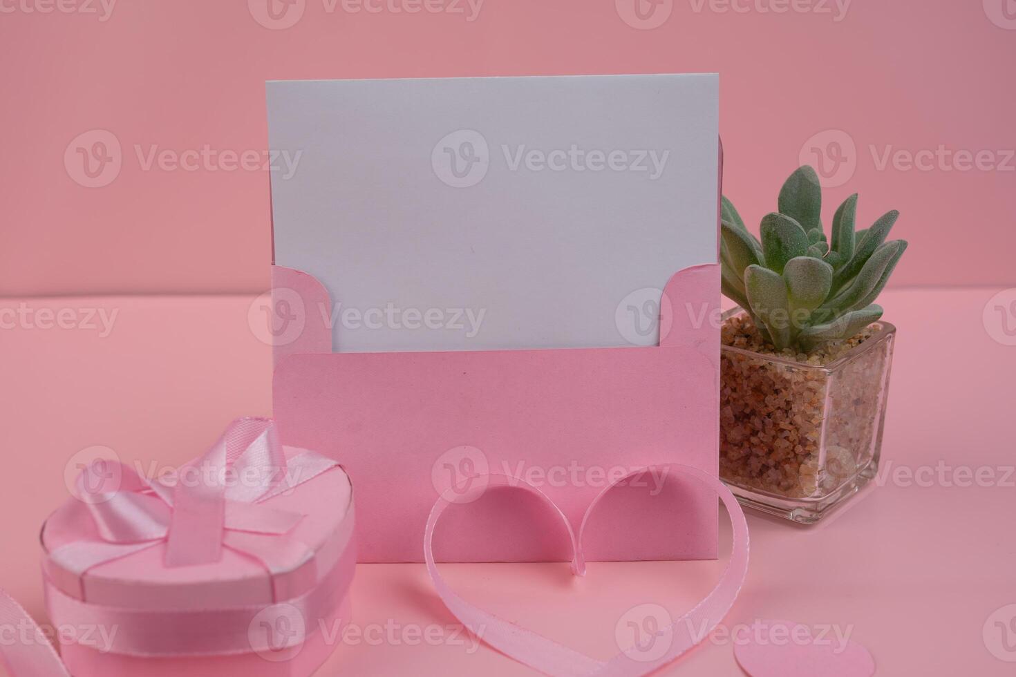 A pink card stands with a heart shaped ribbon and a heart shaped gift box. invitation mockup photo