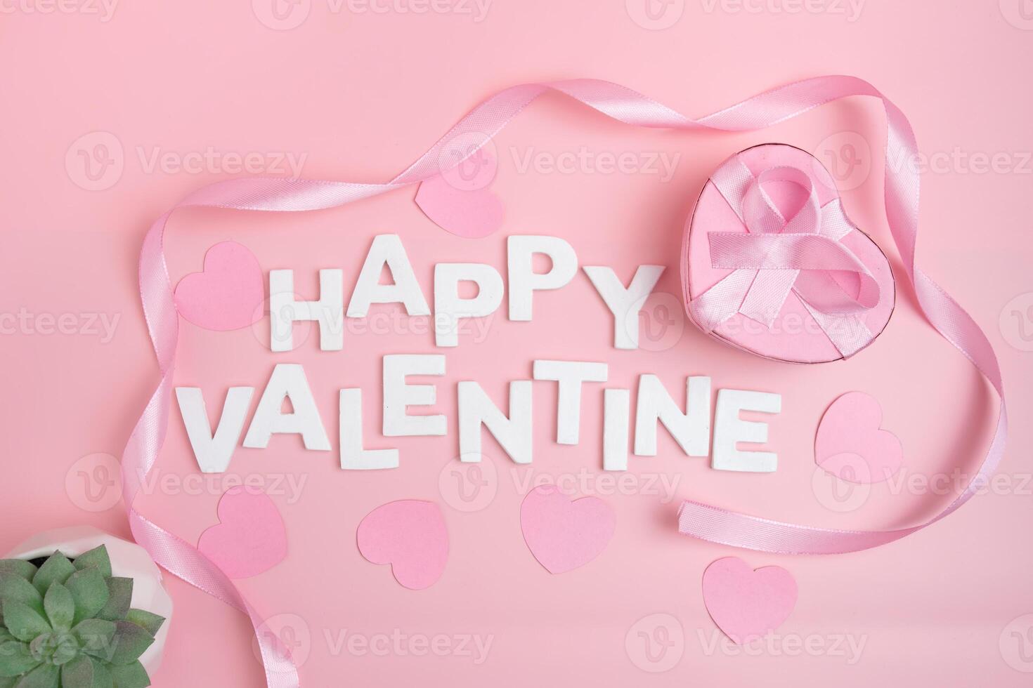 Happy Valentine message spelled out with white letters surrounded by pink hearts and ribbon and a heart shaped gift box photo