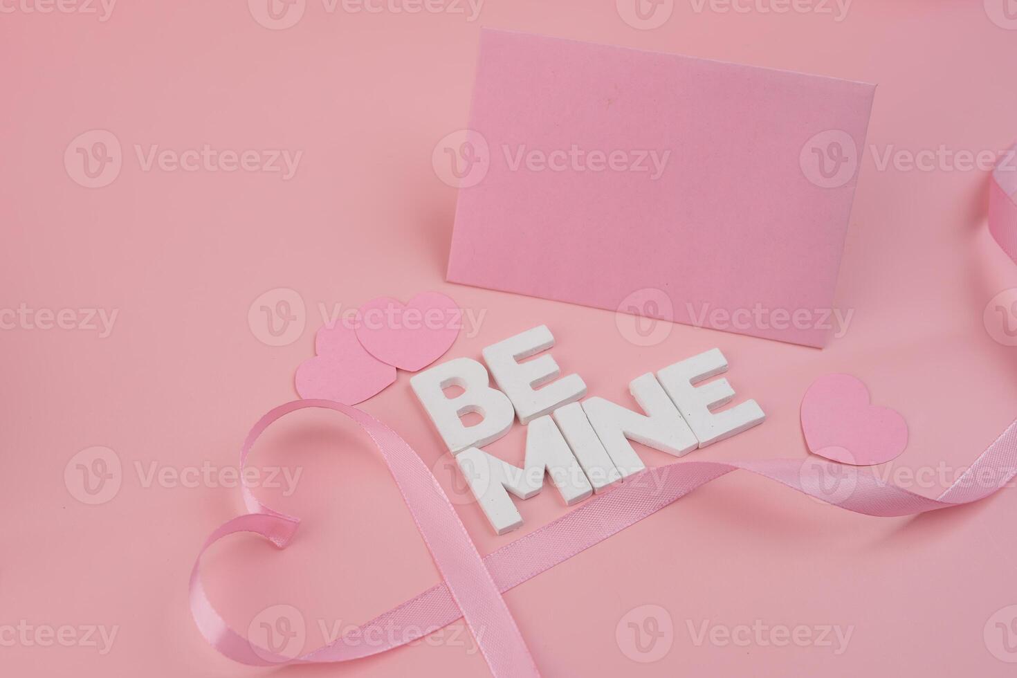 Pink hearts and ribbon arranged around a pink card and the words Be Mine photo