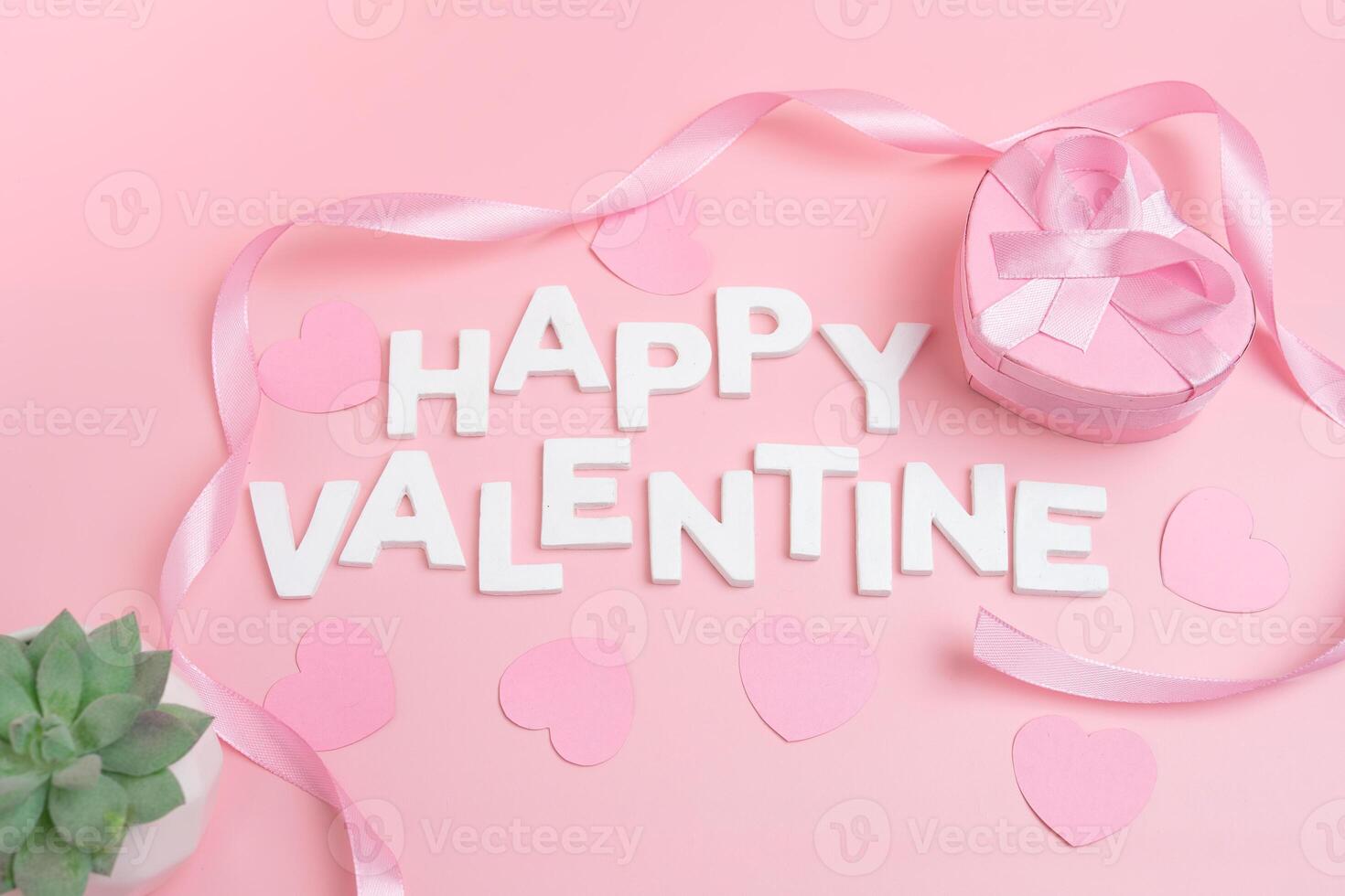 Happy Valentine message spelled out with letters a heart shaped gift box with a ribbon and small hearts scattered around photo