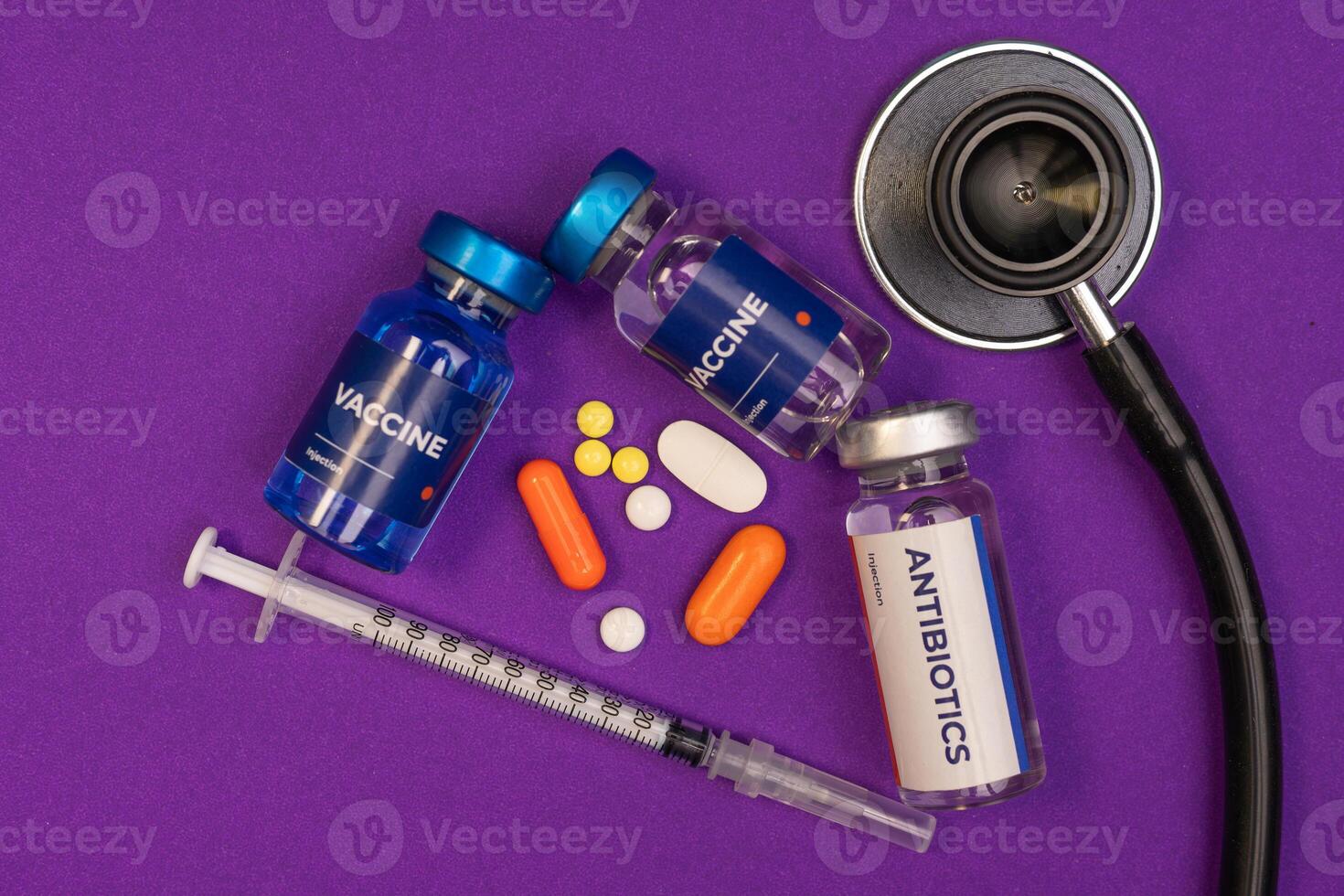 Two vaccine vials one antibiotics vial a syringe pills and a stethoscope lie on a purple surface. health and medical concept photo