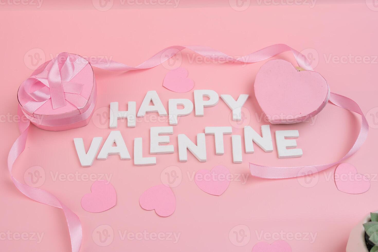 Happy Valentine s Day message spelled out with white letters surrounded by pink hearts ribbon and a pink heart shaped gift box photo