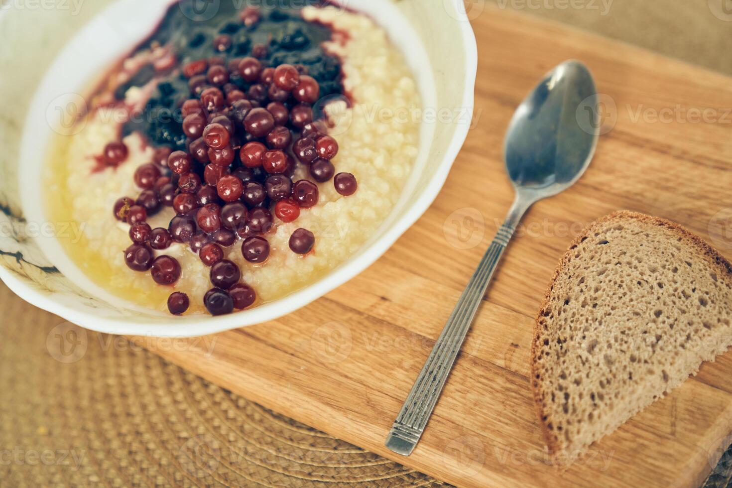 Millet for breakfast. There is a warm wheat porridge with red currants and blueberry jam on the table. A plate of wheat porridge for a healthy gluten-free breakfast. photo