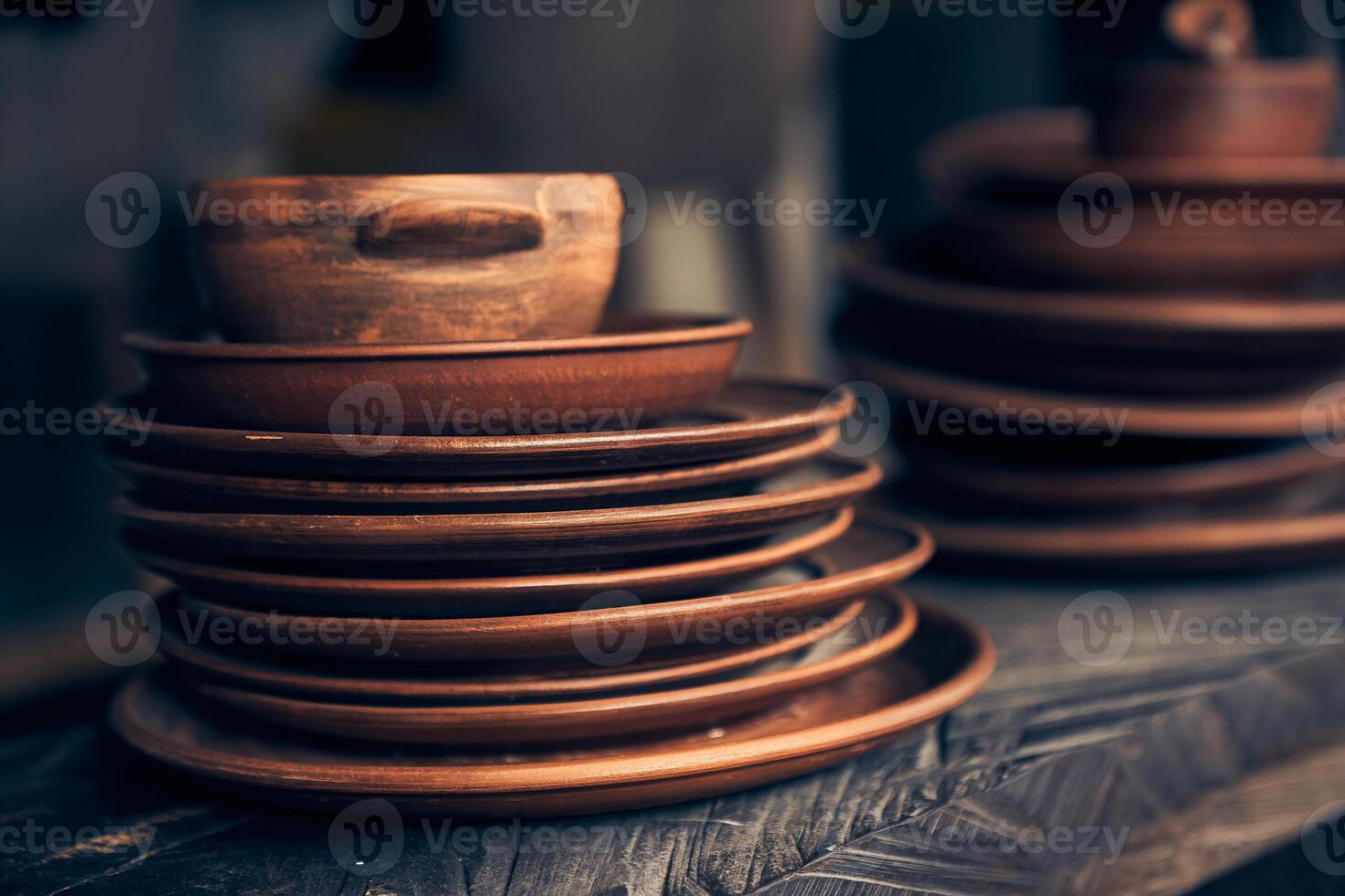 A stack of clay plates of different sizes on a dark background. Level position, top view. Brown plates are on a wooden shelf photo