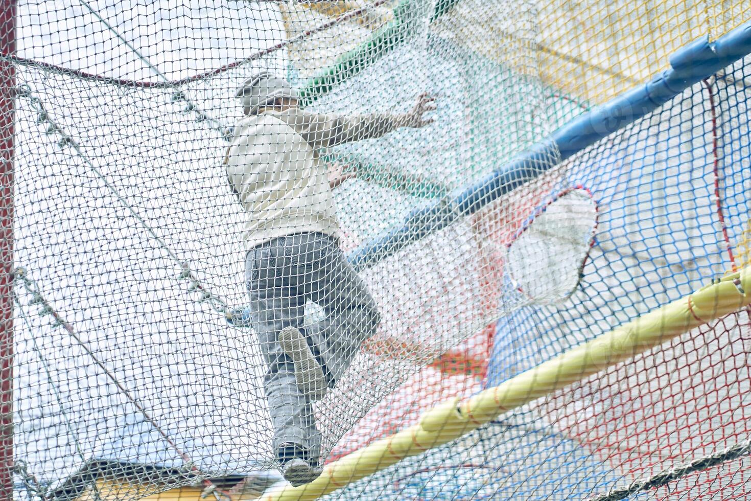 A girl jumps through a mesh maze against the sky in the outdoors. A children's amusement park in the play center with a playground for copying. photo