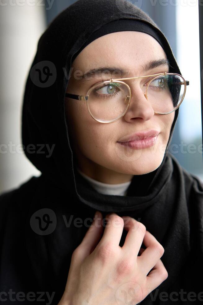 A stunning Muslim businesswoman is captured in a close-up portrait, showcasing her captivating green eyes behind stylish prescription glasses, radiating elegance and confidence photo