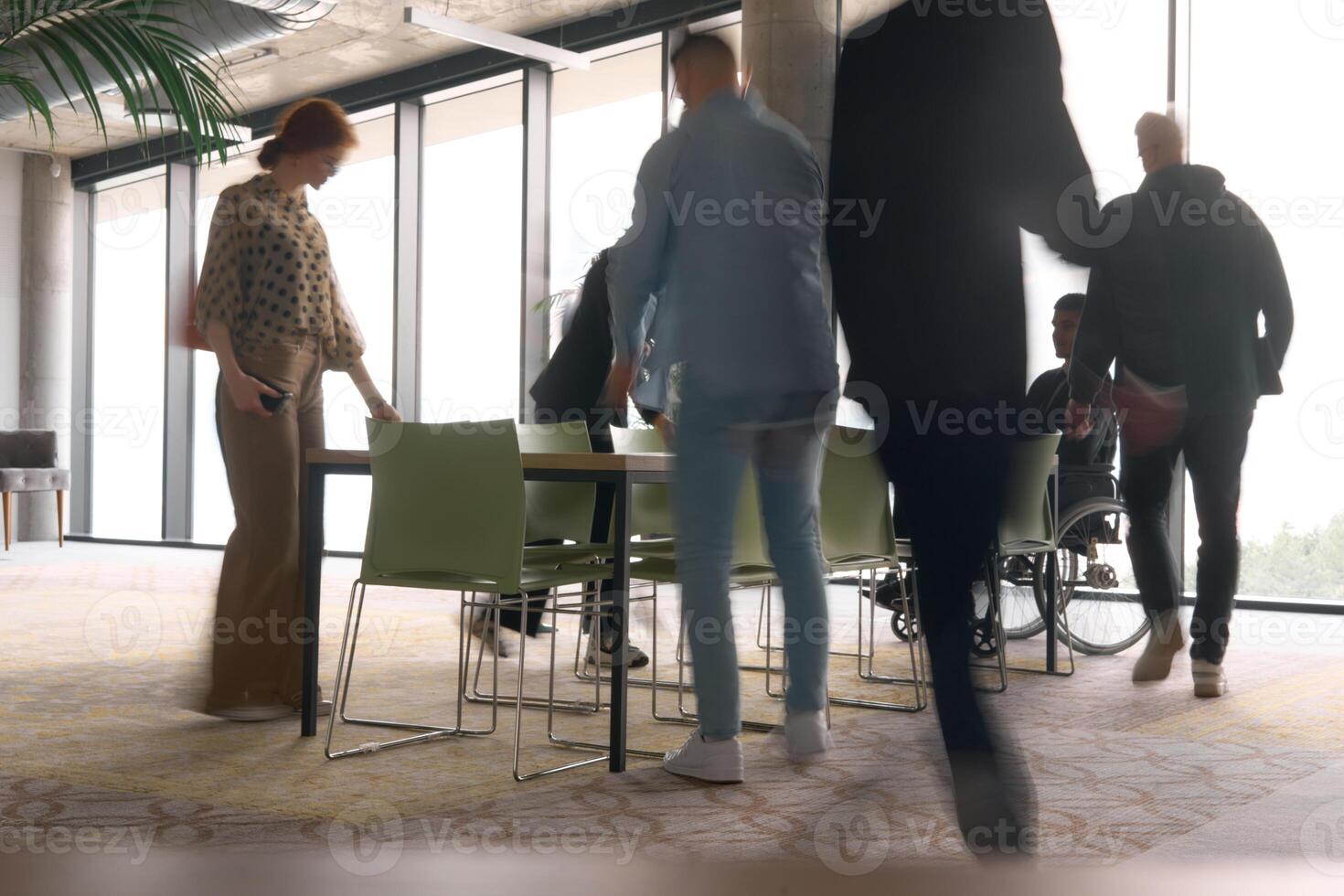 A diverse business team, working urgently around a conference table, collaborates on a meeting while their director, seated in a wheelchair, waits for their input photo