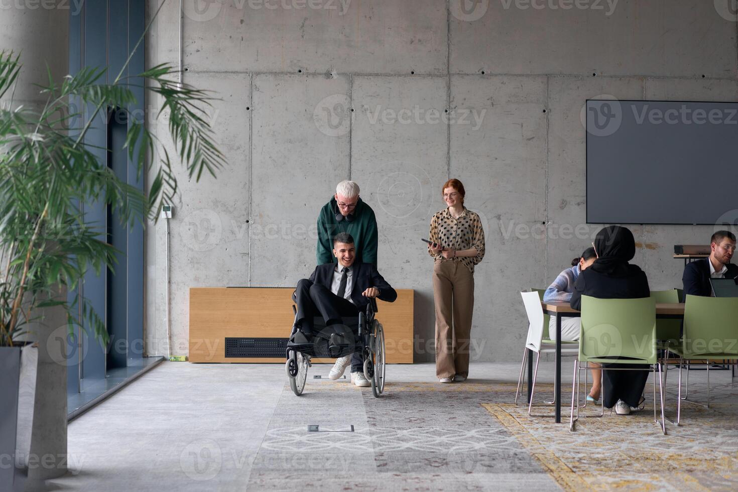 A diverse team of business colleagues, including a director in a wheelchair, engages in a collaborative discussion as they move together through a modern office space photo