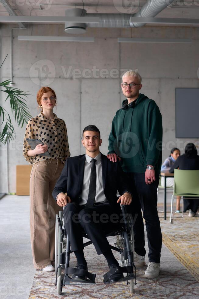 Group cheerful business colleagues, including a businessman in a wheelchair, posing together in a modern office, showcasing teamwork and inclusivity photo