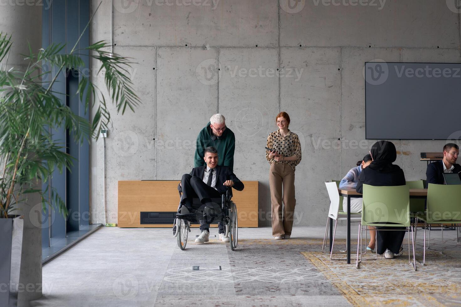 A diverse team of business colleagues, including a director in a wheelchair, engages in a collaborative discussion as they move together through a modern office space photo