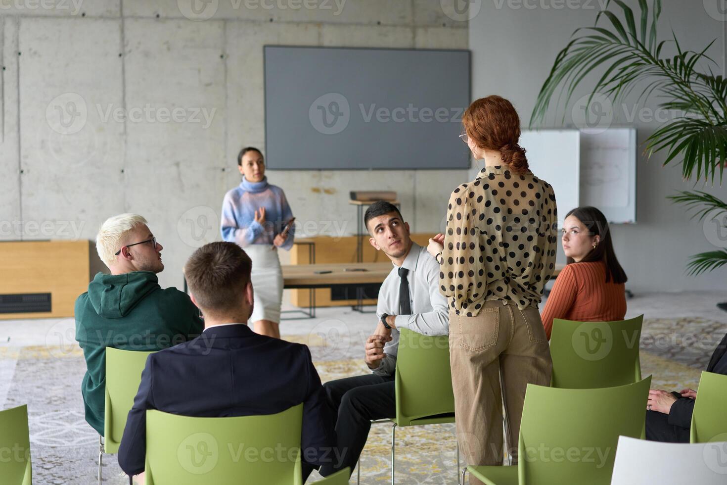 A diverse group of business professionals sits attentively in a modern office, actively participating in a training session led by an instructor, focusing on the latest technological advancements in photo