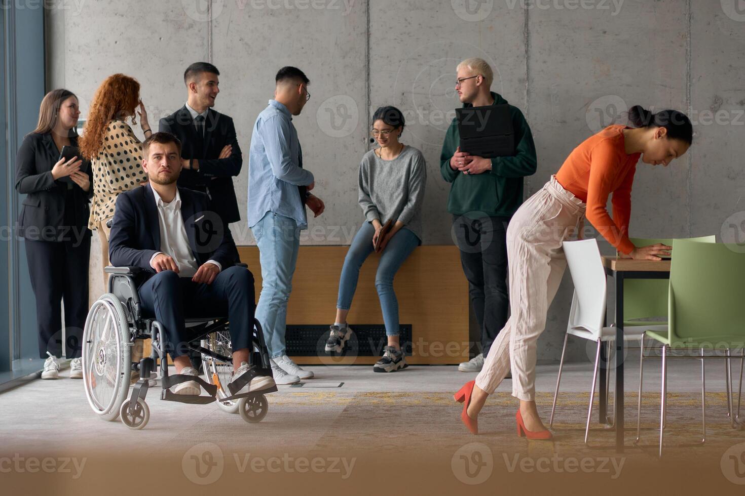 A diverse team of business professionals in a modern office stands alongside their director in a wheelchair, embodying inclusivity, collaboration, and leadership in the workplace photo