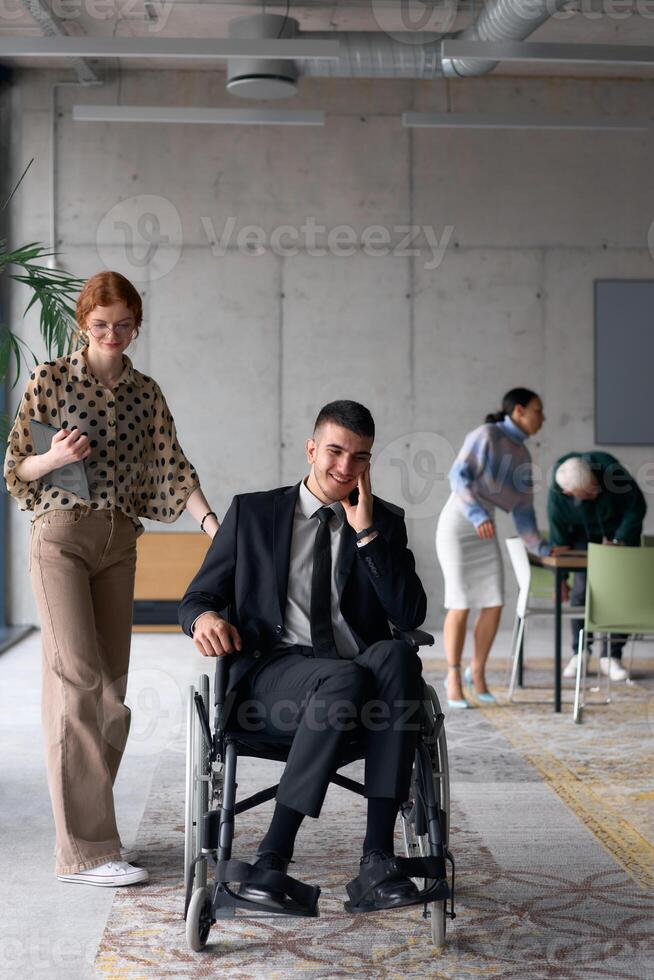 Group cheerful business colleagues, including a businessman in a wheelchair, posing together in a modern office, showcasing teamwork and inclusivity photo