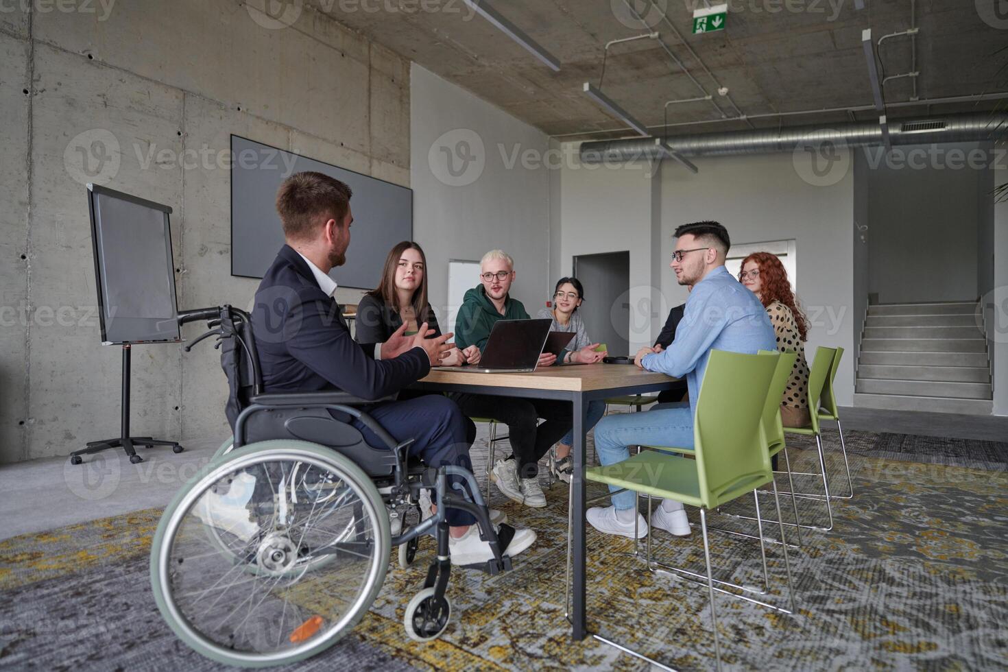 A diverse group of business professionals, including a man in a wheelchair, collaborate during a meeting in a modern office environment. photo