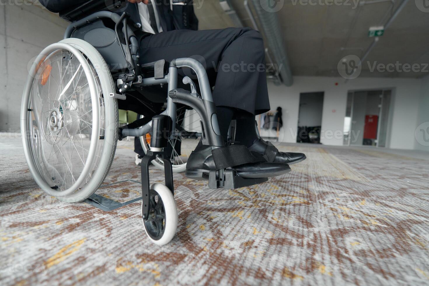 A businessman in a wheelchair enjoys a moment of laughter by a large window in a modern office, embodying positivity, resilience, and a balanced approach to work and life. photo