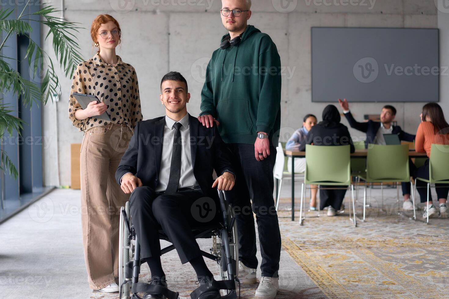 Group cheerful business colleagues, including a businessman in a wheelchair, posing together in a modern office, showcasing teamwork and inclusivity photo
