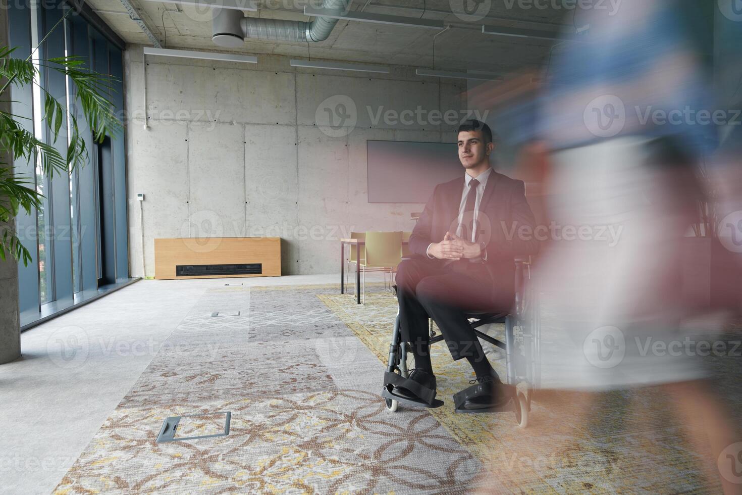 A businessman in a wheelchair navigating through a busy office, surrounded by his colleagues who are actively engaged in their work and collaboration photo
