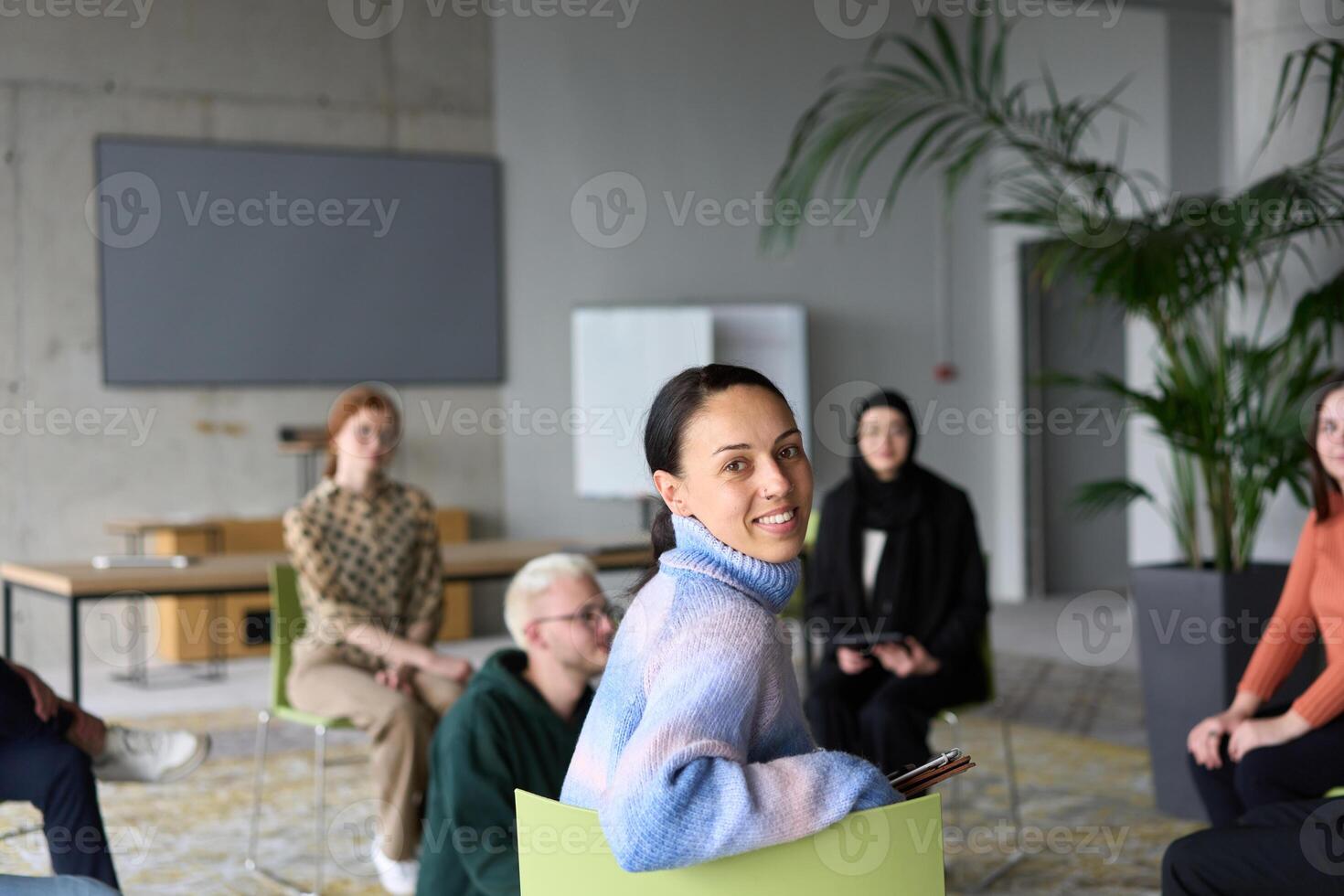A diverse group of business professionals sits attentively in a modern office, actively participating in a training session led by an instructor, focusing on the latest technological advancements in photo