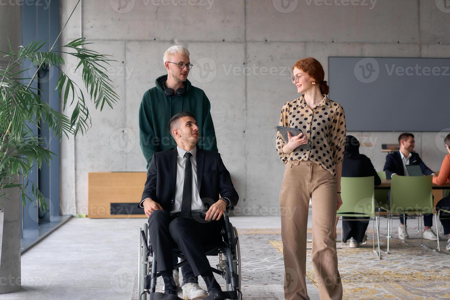 A diverse team of business colleagues, including a director in a wheelchair, engages in a collaborative discussion as they move together through a modern office space photo
