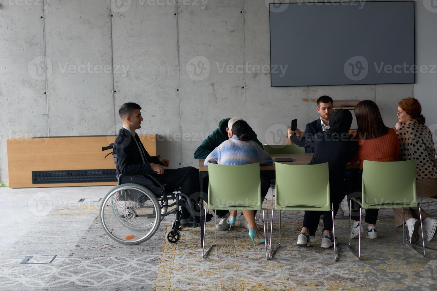 A diverse group of business professionals, including a man in a wheelchair, collaborate during a meeting in a modern office environment. photo
