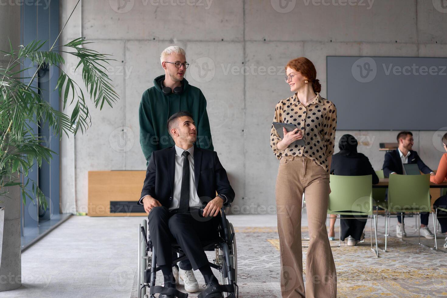 A diverse team of business colleagues, including a director in a wheelchair, engages in a collaborative discussion as they move together through a modern office space photo