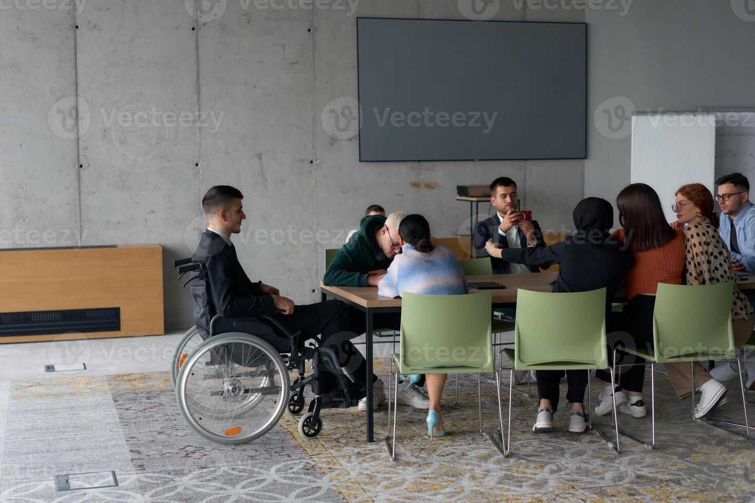 A diverse group of business professionals, including a man in a wheelchair, collaborate during a meeting in a modern office environment. photo